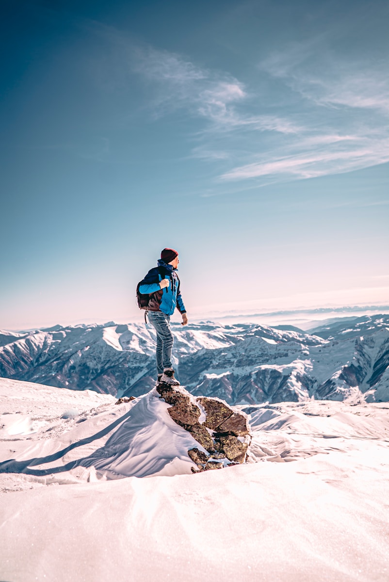 man in black jacket and blue denim jeans standing on snow covered mountain during daytime